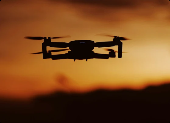 A drone silhouetted against an orange sunset sky